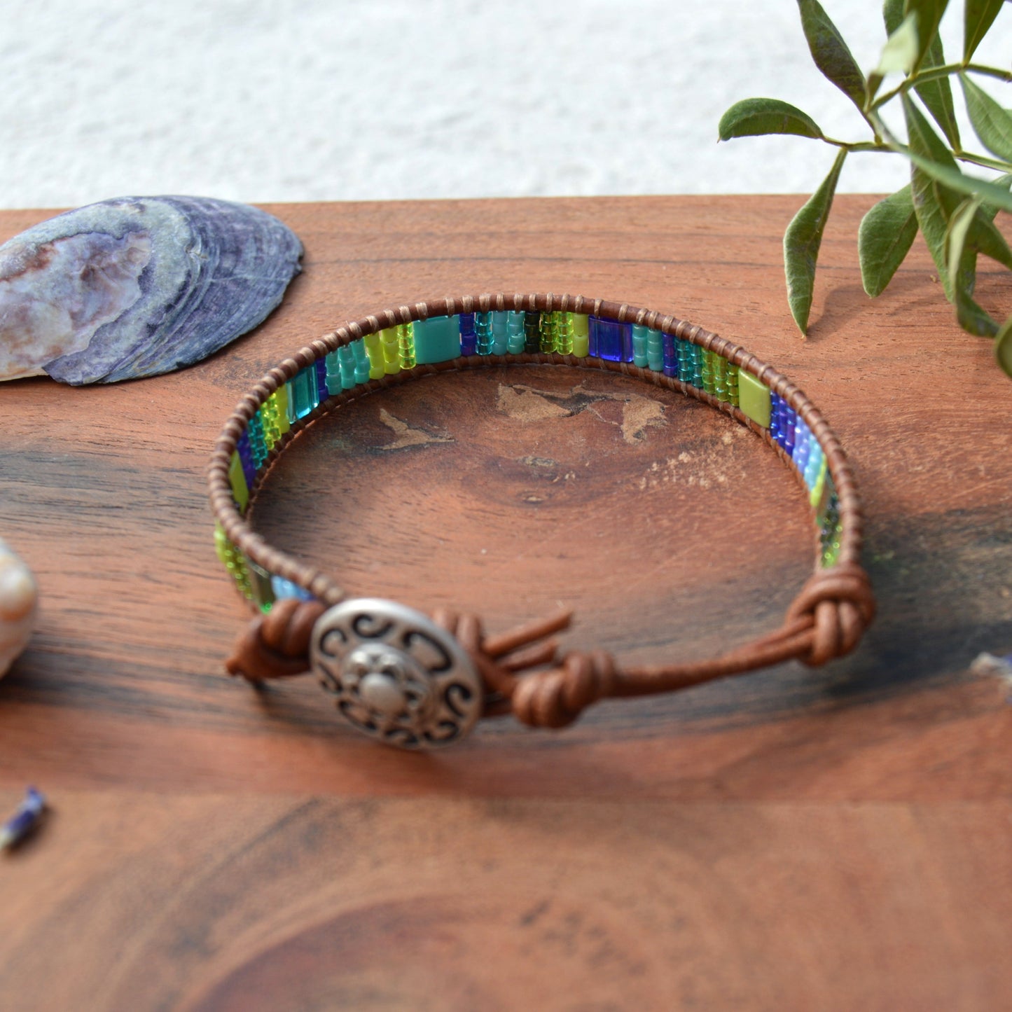 Leather wrap bracelet in green and blue tones with decorative button as a lock and extension chain in leather.