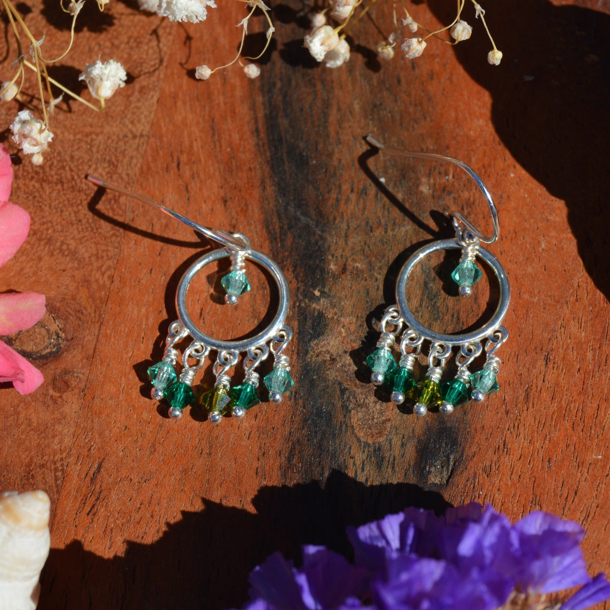 A pair of silver hoop dangle earrings with green and turquoise Czech faceted bicones. 