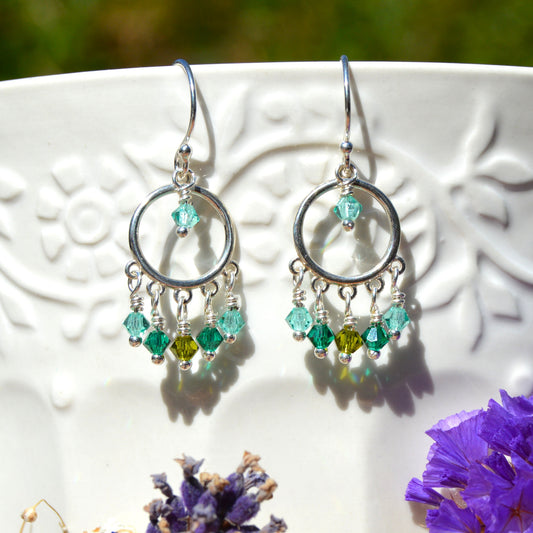 A pair of silver hoop dangle earrings with green and turquoise Czech faceted bicones.
