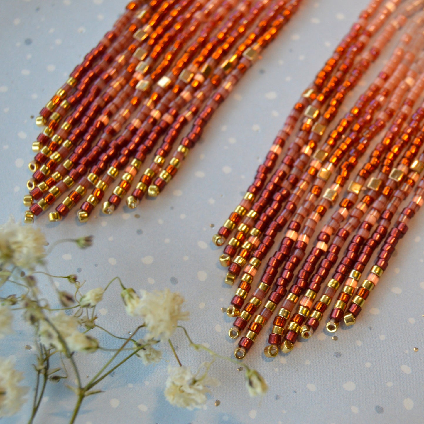 Dreaming Big long fringe earrings made of high quality Japanese seed beads in pink, dark orange, and shades of bordeaux colour combined with gold.