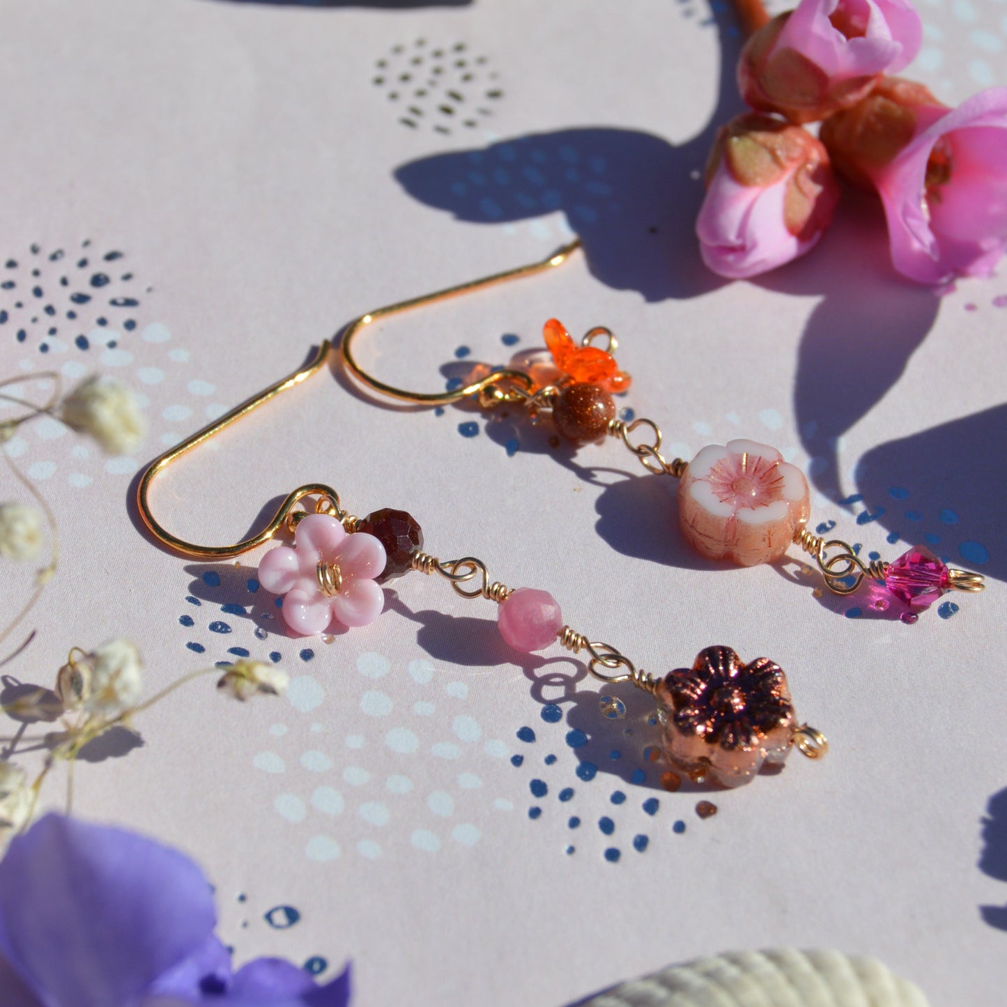 Gold-plated sterling silver earrings featuring Czech glass flowers, lampwork flowers, gemstones, and a bicone. Sold by piece.