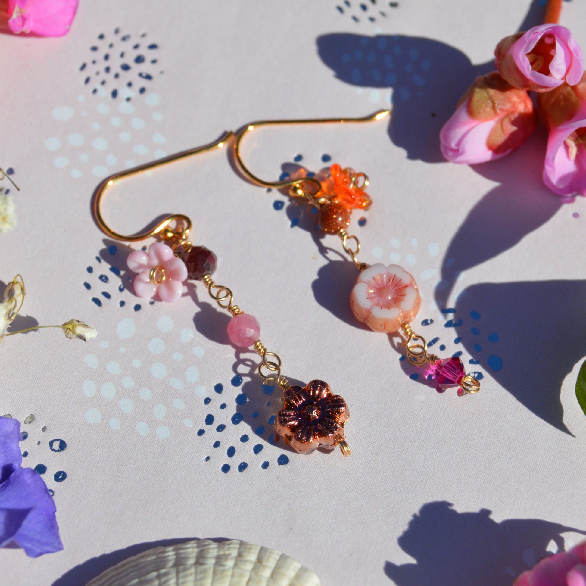 Gold-plated sterling silver earrings featuring Czech glass flowers, lampwork flowers, gemstones, and a bicone. Sold by piece.