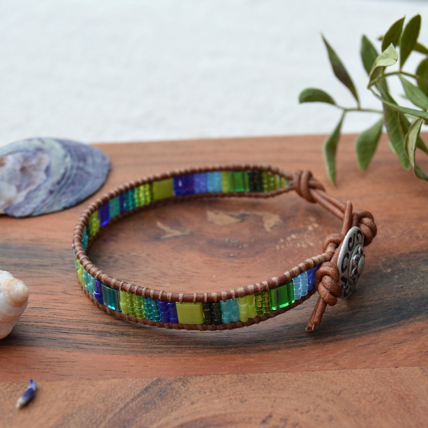 Leather wrap bracelet in green and blue tones with decorative button as a lock and extension chain in leather.